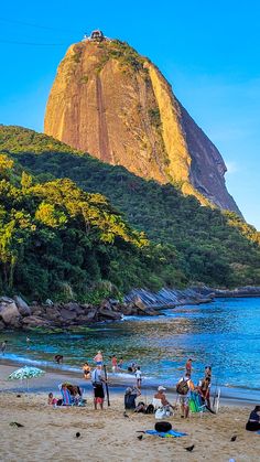 many people are on the beach with mountains in the backgrouds and blue water