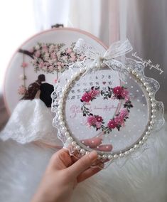 a person holding up a small clock with flowers and pearls on the frame in front of a mirror