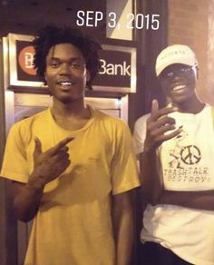 two young men standing next to each other in front of a bank booth with their fingers up