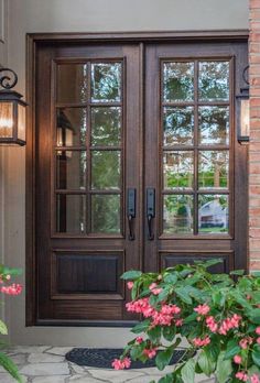 a pair of double doors with sidelights on the front of a house next to pink flowers