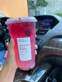 a person holding up a pink drink in their hand while sitting in the driver's seat of a car