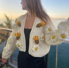 a woman standing next to a railing wearing a sweater with bees on it