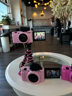 three pink cameras sitting on top of a white table next to a camera tripod