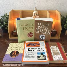 several books are sitting on a table with a buddha figurine in the background