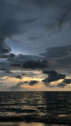 the sun is setting over the ocean with dark clouds in the sky and some water