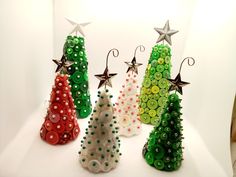 four different colored christmas trees made out of buttons and plastic beads on a white surface