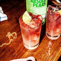 two cocktails on a wooden table next to a bottle of absolus pears