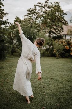 a woman in a white dress standing on one leg and reaching up to the sky