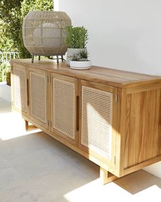 a wooden sideboard sitting on top of a white floor next to a potted plant