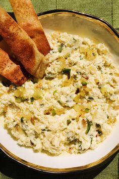 a bowl filled with food sitting on top of a green table cloth next to bread sticks