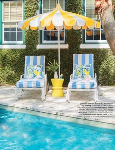 two lawn chairs under an umbrella next to a swimming pool in front of a house