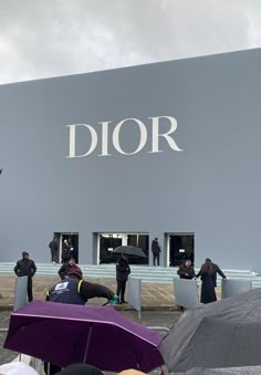 many people are standing in front of a dior store with their umbrellas open