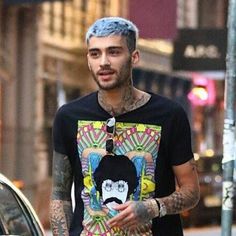 a man with blue hair is walking down the street wearing a t - shirt that has a cartoon character on it