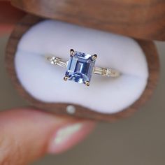 a person holding an engagement ring with a blue stone in it's center and two white diamonds on the side