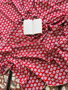 an open book laying on top of a red and white patterned cloth covered in circles