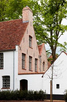 an old white house with a red roof and brown shingles on the top floor