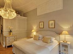 a bed room with a neatly made bed and a chandelier hanging from the ceiling