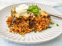 a white plate topped with rice covered in sauce and green peppers next to a fork