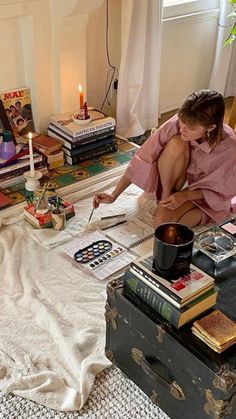 a woman sitting on top of a bed next to a table filled with books and candles