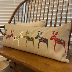 a pillow with reindeers on it sitting on a wooden bench next to a window