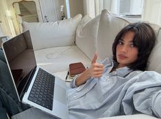 a woman sitting on a couch with a laptop in her lap giving the thumbs up sign