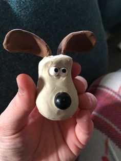 a hand holding a clay dog with fake ears and eyes on it's face