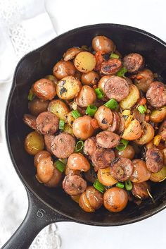 a skillet filled with sausage and potatoes on top of a white table next to a napkin