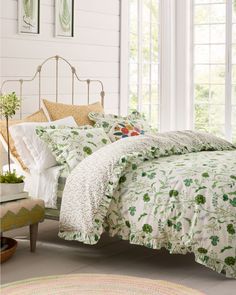 a bed with green and white comforters in a room next to windows, rugs and pictures on the wall