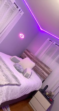 a white bed sitting in a bedroom next to a purple light on the side of a wall