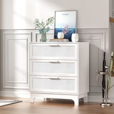 a white dresser with two vases on top of it next to a framed photograph