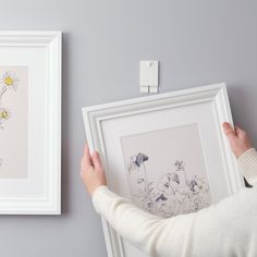 a person holding up a framed flower art print in front of a wall mounted light switch