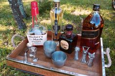 an assortment of liquor bottles and glasses on a wooden tray in front of a tree