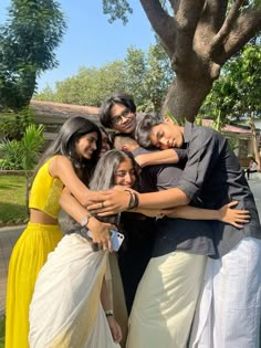 a group of people hugging each other in front of a tree and grass area with trees behind them