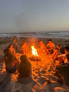 a group of people sitting around a fire on the beach