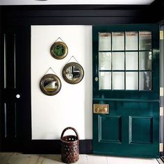 a green door with three mirrors on the wall and a basket in front of it