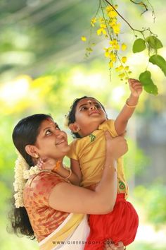 a woman holding a child in her arms and looking up at the sky with yellow flowers on it