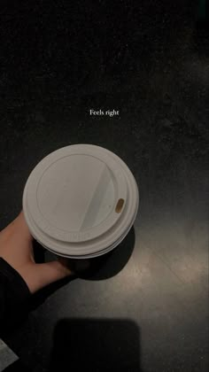 a person is holding a white cup with the lid open on a black countertop