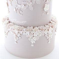 a three tiered wedding cake with white flowers on the top and bottom layer is decorated with lace