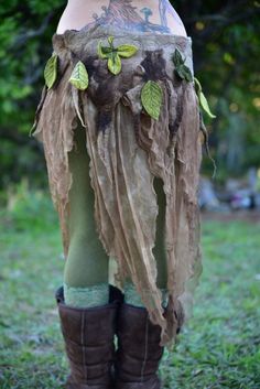 a woman with tattoos wearing a skirt made out of paper and leaves on her legs