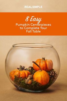 a glass bowl filled with pumpkins on top of a table next to pine cones