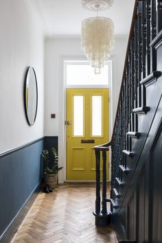 a yellow door and some black stairs in a room with white walls, wood floors and a chandelier hanging from the ceiling