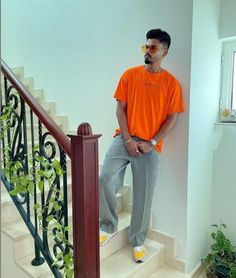 a man in an orange shirt is standing on the stairs with his hands behind his back