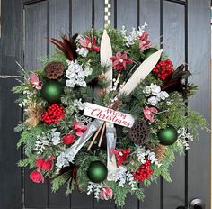 a christmas wreath hanging on the front door with evergreens, pine cones and feathers