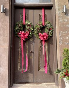 two wreaths on the front door of a building with pink ribbons tied around them