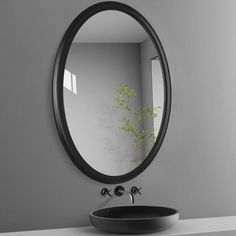 a round mirror hanging on the wall above a sink with a black bowl underneath it