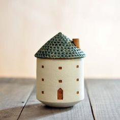 a small white ceramic house with a green roof on a wooden table in front of a wall