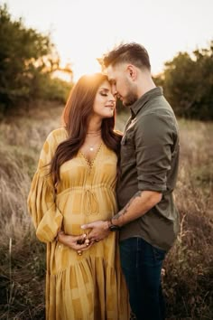 a pregnant couple standing in the grass at sunset