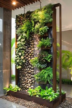 an outdoor garden with lots of plants and rocks on the wall, along with water running down it