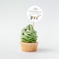 a cupcake with green frosting sitting on top of a white table next to a sign that says, little fishermanman is on the way