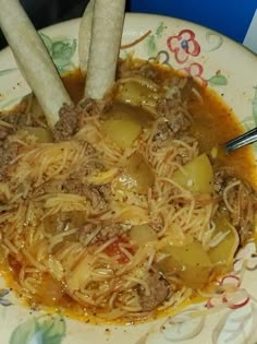 a bowl filled with noodles and meat on top of a floral design plate next to two hot dogs